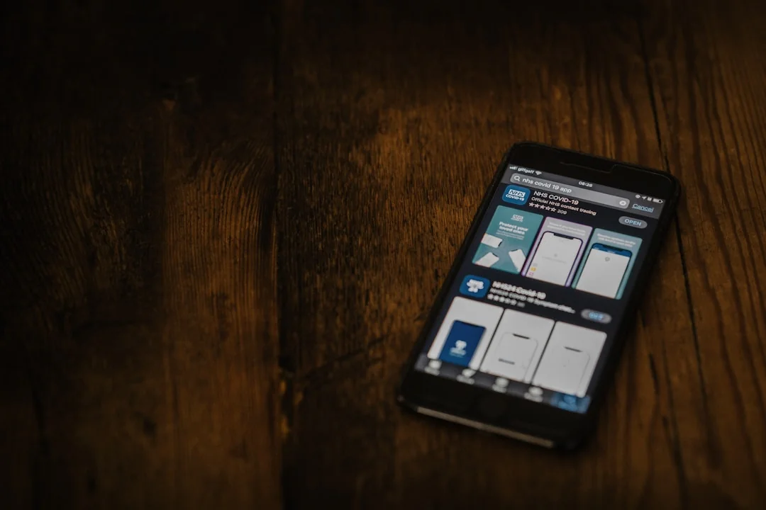 Hand holding smartphone displaying digital wallet app interface, blurred monitor in background.